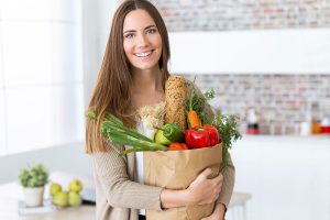 Beautiful young woman with vegetables in grocery bag at home.